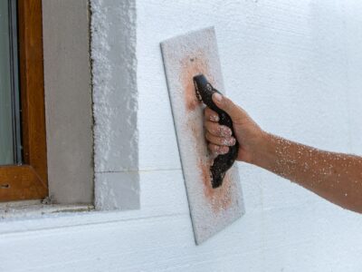 Hand of a worker with a tool for sanding and making smooth and even the surface of a house wall